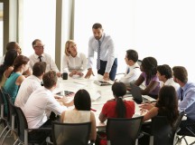 Businessman Addressing Meeting Around Boardroom Table